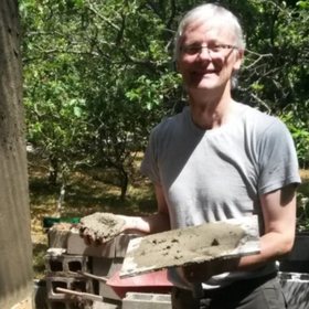 John Rogers holding a trowel and a block of cob in an orchard