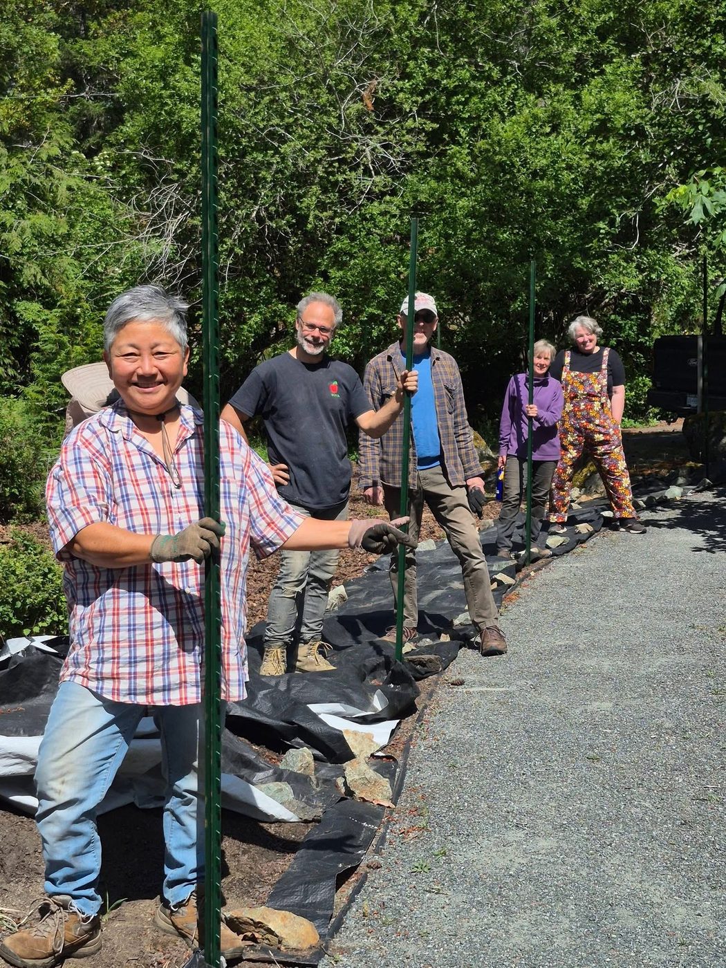A row of smiling Highlands volunteers holding fence posts along the community garden work-party line