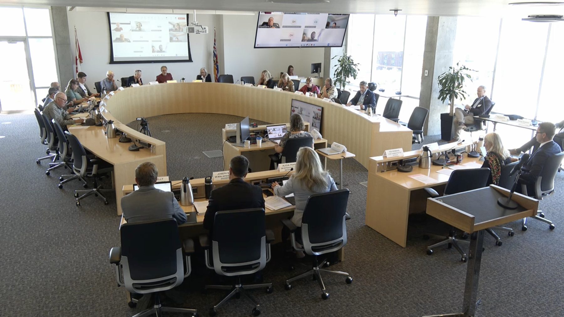 The CRD Regional Water Supply Commission meeting around its horseshoe table, with BC and Canadian flags and hybrid video participants on screen