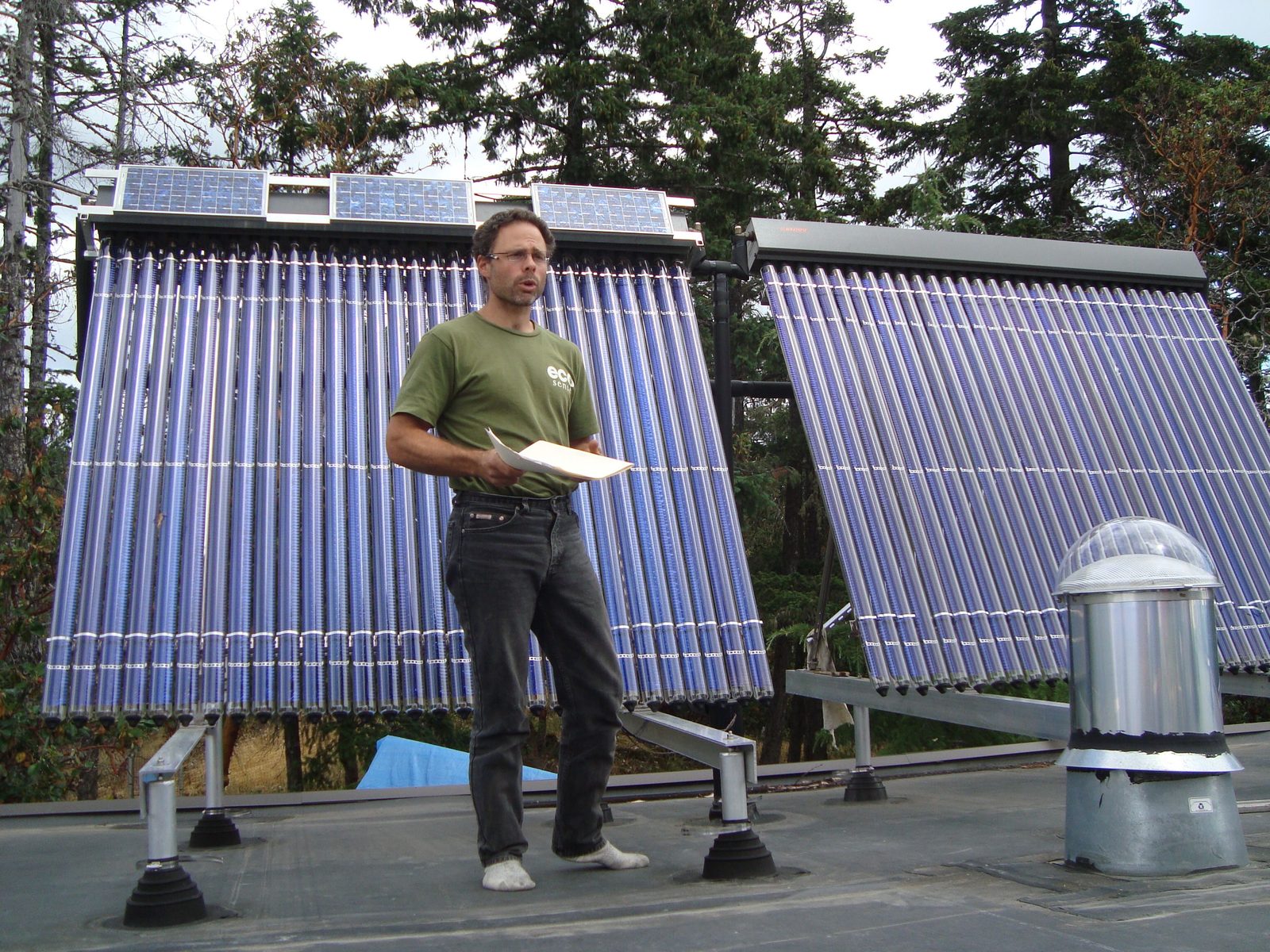 Gord Baird teaching a group on the Eco-Sense rooftop, standing between two large solar hot-water arrays